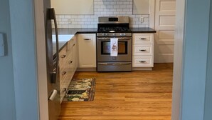 Une cuisine avec des armoires blanches, une cuisinière en acier inoxydable et un plancher en bois.