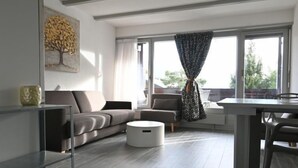 Ein modernes Wohnzimmer mit einem grauen Sofa, einem runden weißen Hocker und einem Esstisch mit Stühlen.