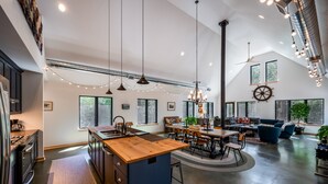 A spacious kitchen with a central island, large windows, and a dining area with a high ceiling and exposed ductwork.