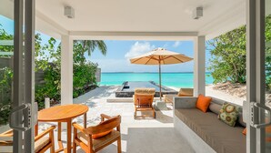 A modern outdoor seating area with a view of the ocean, a wooden table, and a cushioned sofa. - Siyam World Maldives - All-inclusive  (Dhigurah)