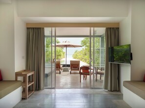 A modern living room with a sliding glass door leading to an outdoor seating area with a table and chairs, a TV mounted on the wall, and a wooden bench.