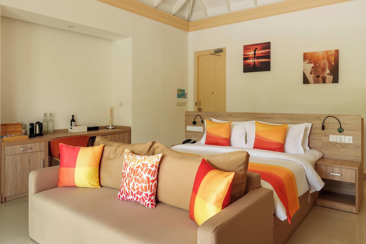 A hotel room with a bed, a sofa, a wooden nightstand, a desk, and a wardrobe.