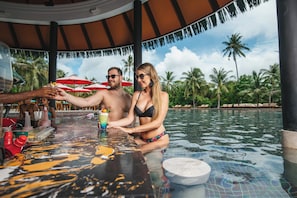 A couple in a poolside bar area with a tropical backdrop.