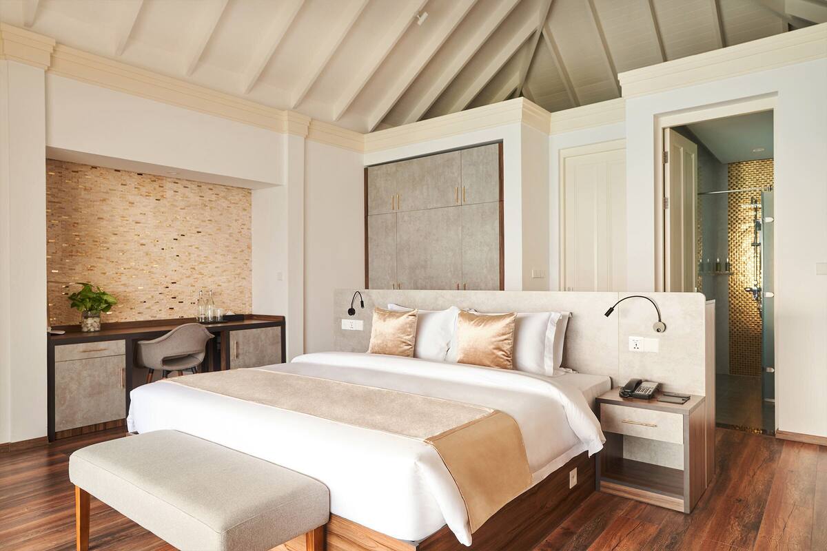 A modern bedroom with a large bed, bedside tables, a desk, and a bathroom visible through an open door.