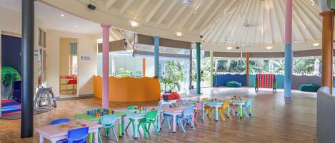 A spacious indoor area with multiple tables and chairs, a play area, and a view of the outdoors.