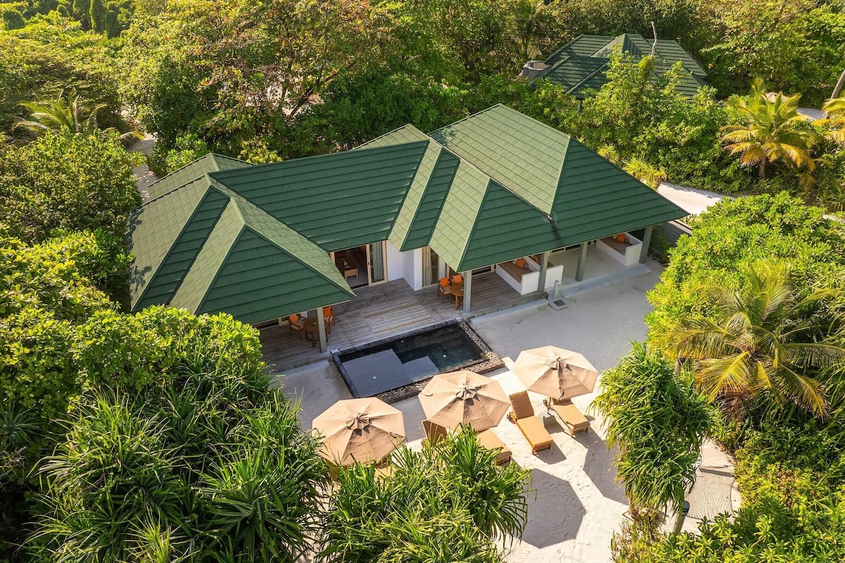 A resort with multiple green-roofed buildings surrounded by lush greenery and a swimming pool area with umbrellas.