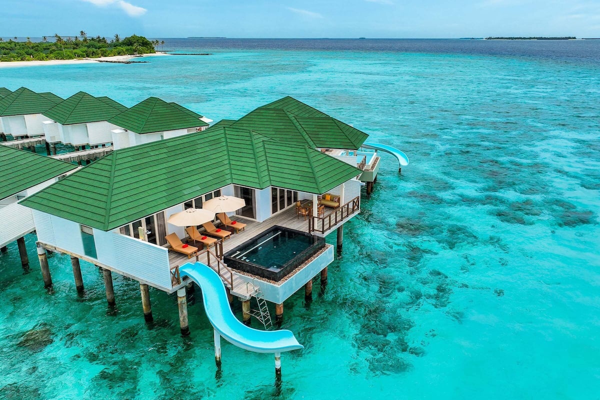 Overwater bungalows with a pool, lounge chairs, and a slide.