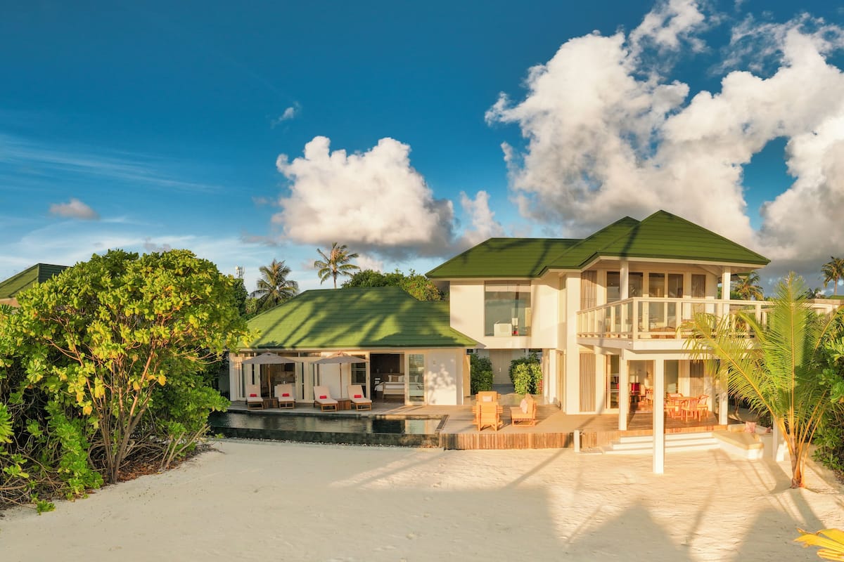 A two-story beachfront house with a covered patio and outdoor seating area.