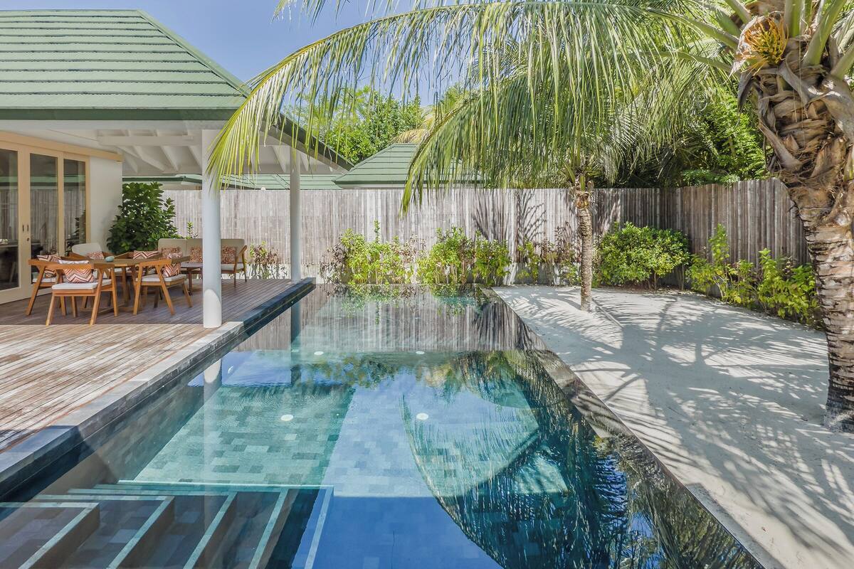 A swimming pool with a wooden deck, a covered patio area, and a wooden fence.