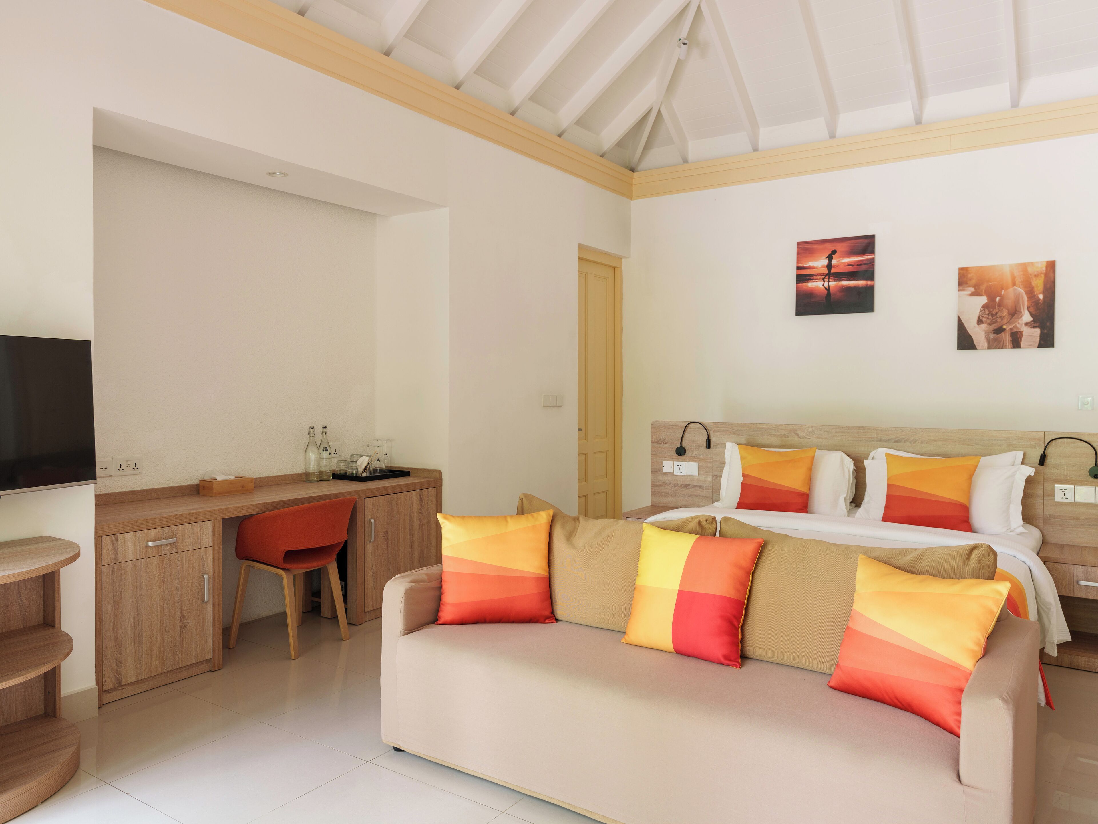 A modern hotel room with a sofa, a desk, and a TV.