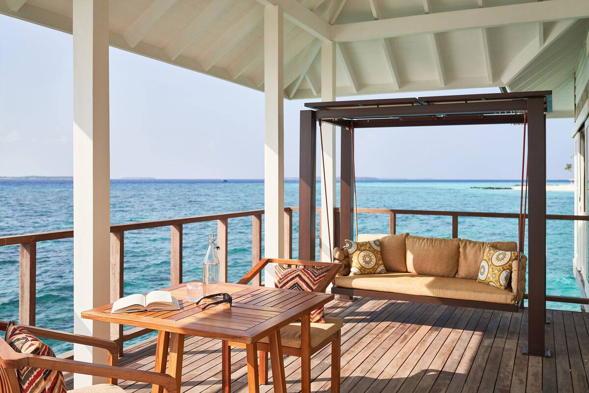 A wooden deck with a table and a sofa facing the ocean.