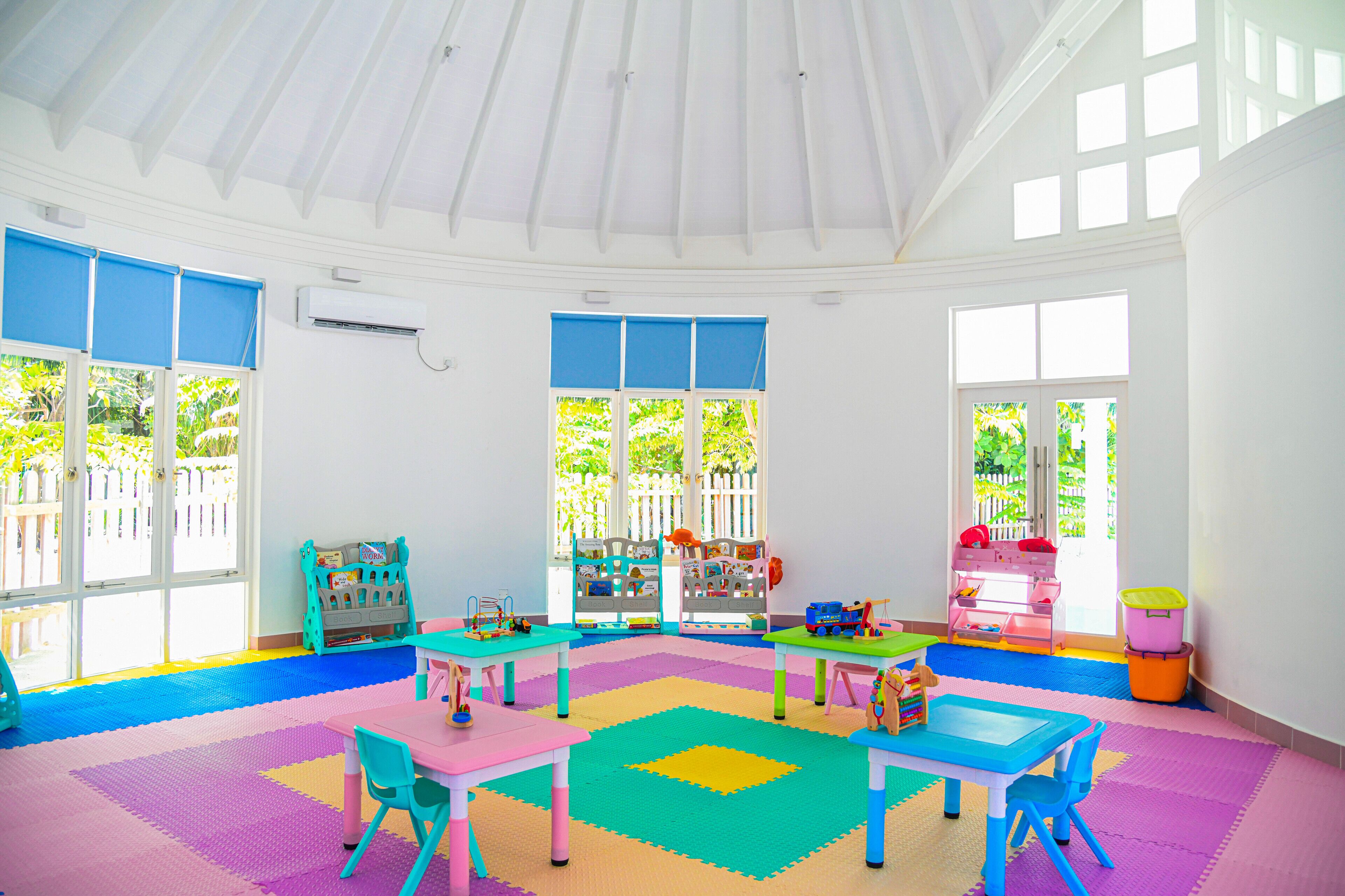 A bright, well-lit room with a high ceiling, large windows, and colorful play mats.
