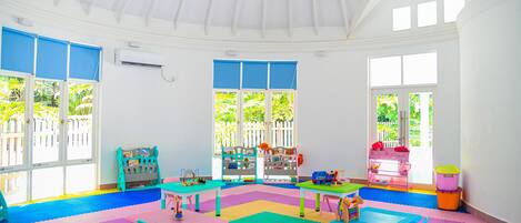 A bright, well-lit room with a high ceiling, large windows, and colorful play mats.