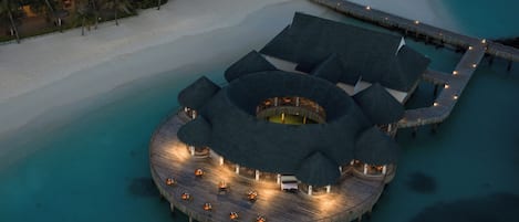 Un resort sobre el agua con una edificación circular, un muelle y una playa.