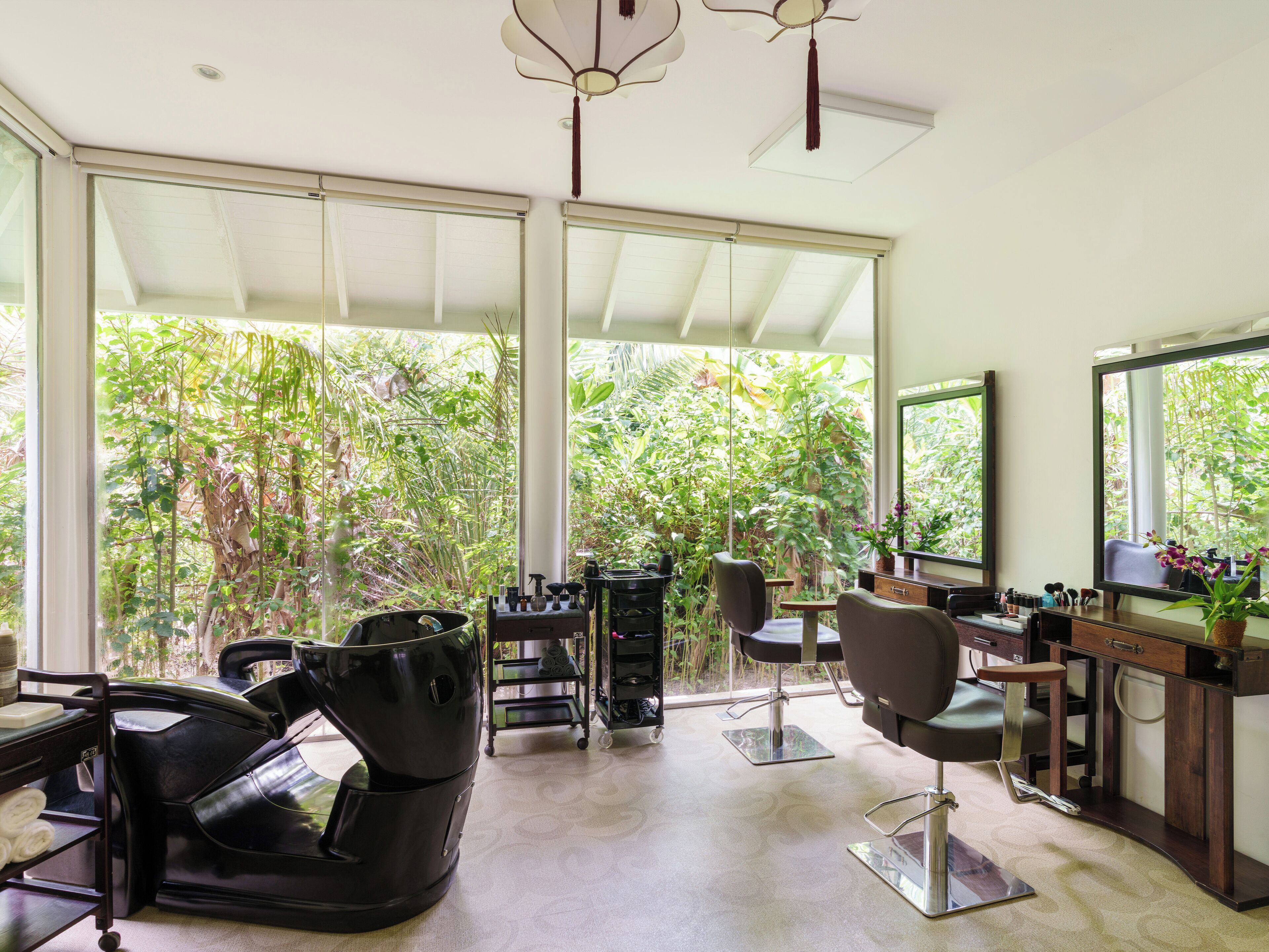 A modern salon with large windows, a black salon chair, a mirror, and a hairdryer.