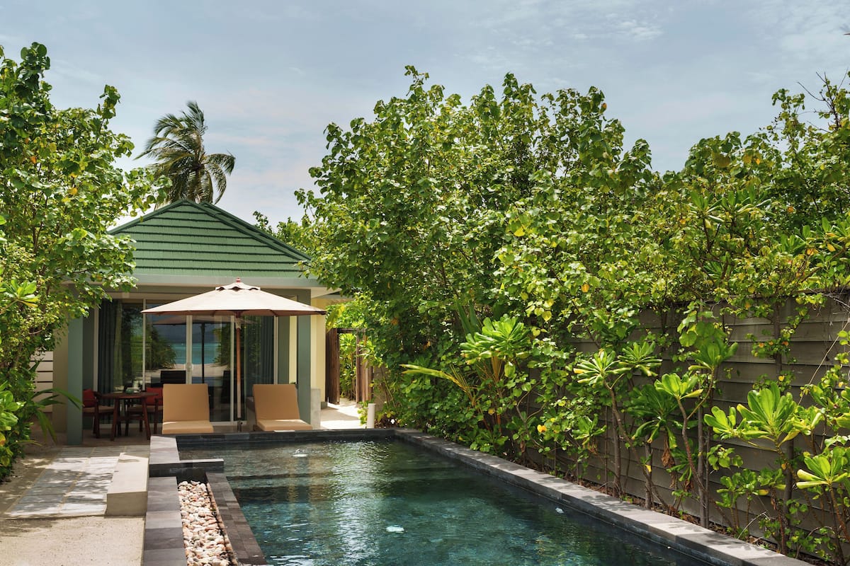 A pool area with a covered seating area and lush greenery.