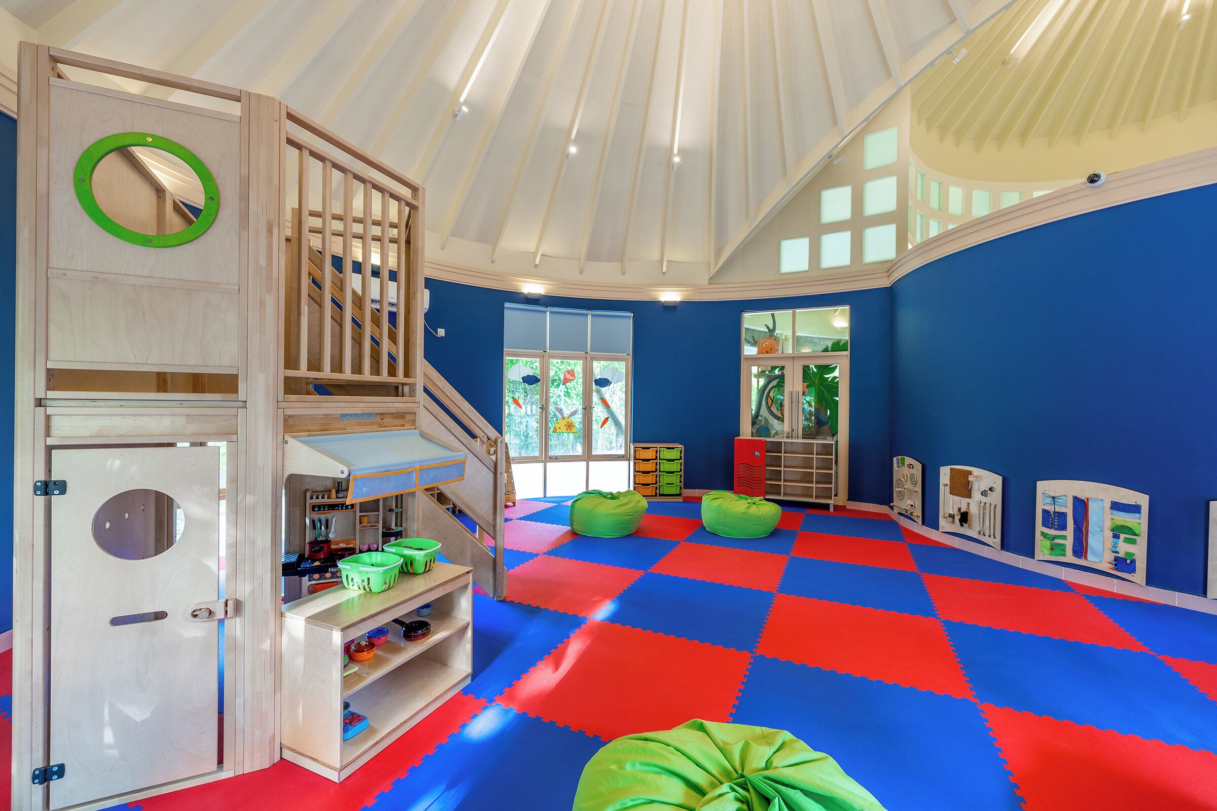 Una sala de juegos infantil con suelo a cuadros, estructuras de madera para jugar y exhibiciones educativas.