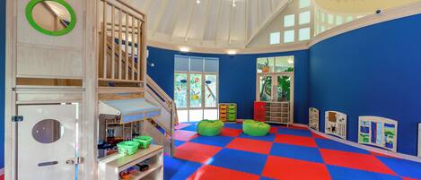 Una sala de juegos infantil con suelo a cuadros, estructuras de madera para jugar y exhibiciones educativas.