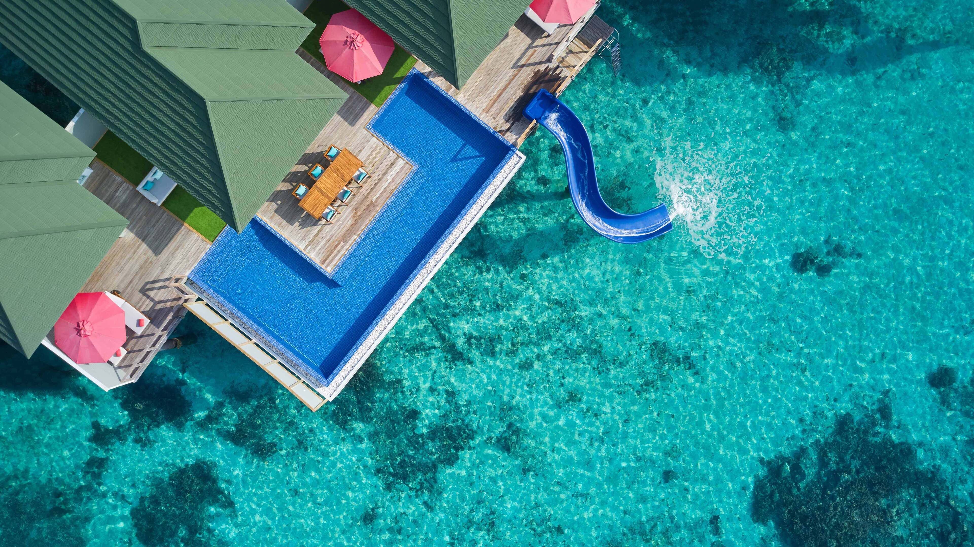 An aerial view of a resort with a swimming pool, lounge chairs, and umbrellas.