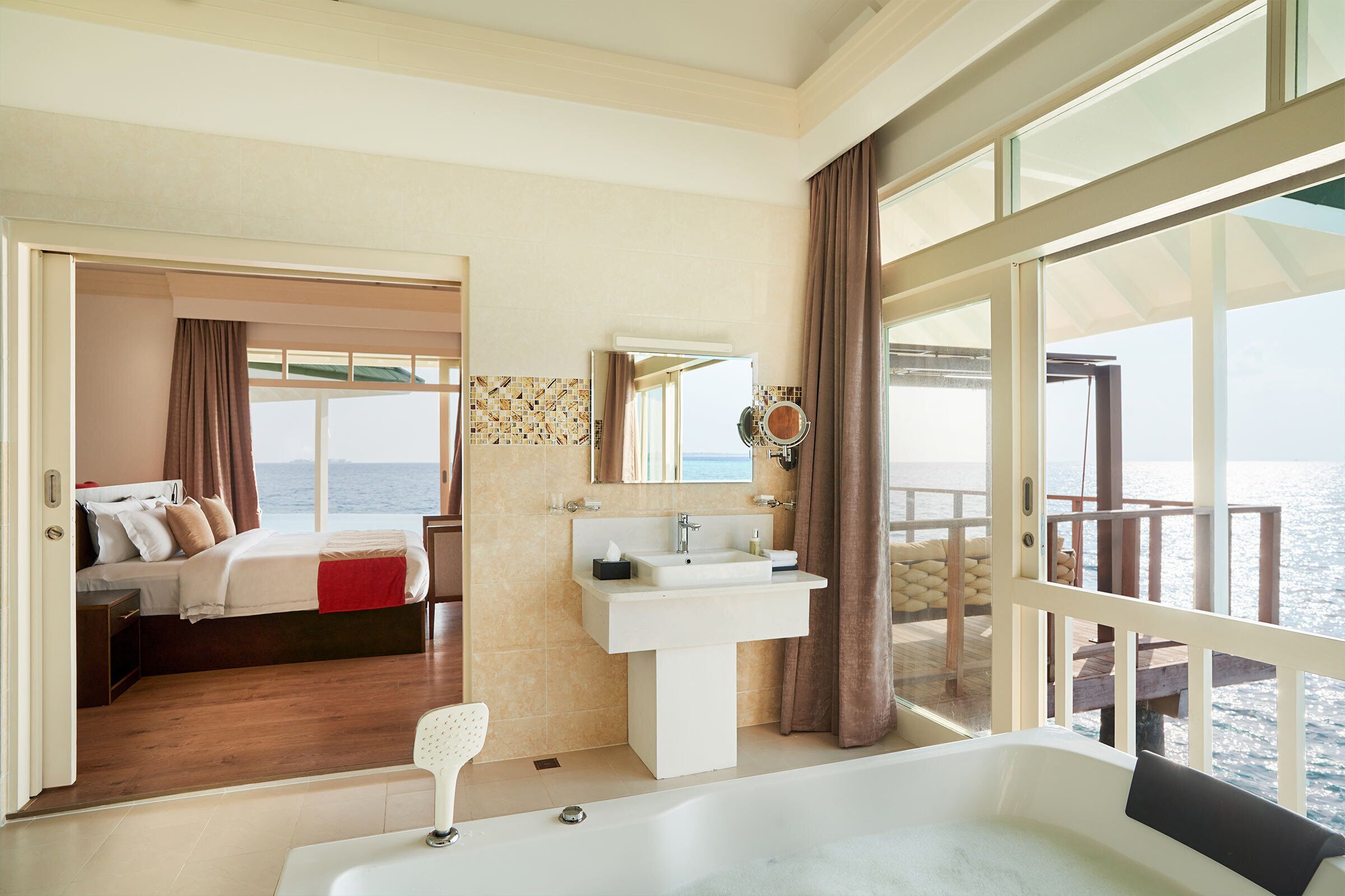 A spacious bedroom with a large window, a private balcony, a bathroom with a bathtub, and a view of the sea.