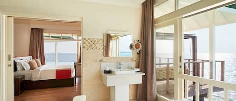 A spacious bedroom with a large window, a private balcony, a bathroom with a bathtub, and a view of the sea.