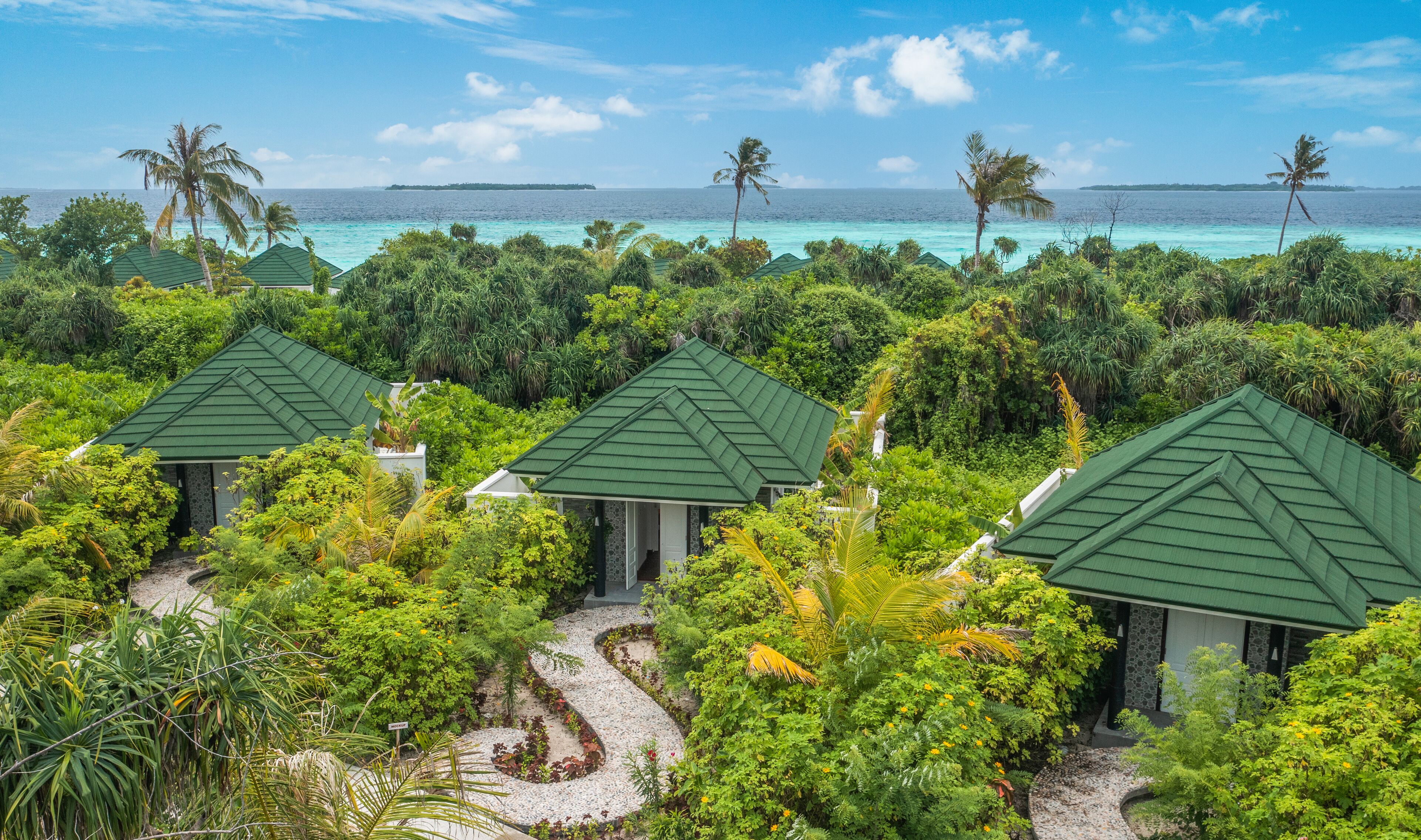 A resort with multiple green-roofed cottages surrounded by lush greenery and a view of the ocean.
