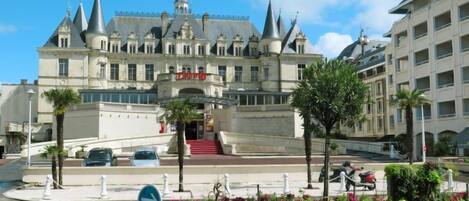 A grand hotel with a prominent entrance, a red staircase, and a landscaped garden with tropical plants.