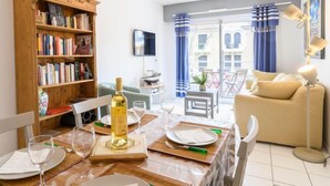 A dining area with a wooden table set for two, a bookshelf, a sofa, and a TV.