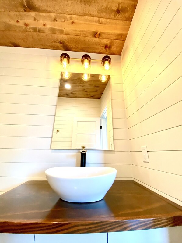 A bathroom with a white sink, wooden ceiling, and a mirror above the sink. - Cozy & Cute Modern Tiny house close to wineries, wedding venues, and outdoor fun (Dripping Springs)