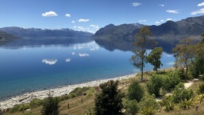 A serene lake with mountains in the background, a clear sky, and a rocky shoreline with sparse vegetation. - Lake Hawea Lakefront Cabin (Lake Hawea)