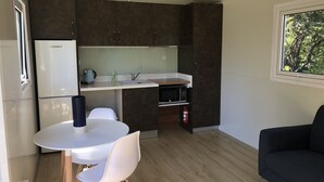 A compact kitchen with dark cabinets, a white countertop, a sink, a microwave, and a small dining area with a white table and chairs. - Lake Hawea Lakefront Cabin (Lake Hawea)