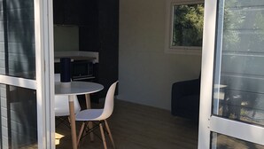 A modern kitchen with dark cabinets, a white countertop, and a small dining area with a white table and chairs. - Lake Hawea Lakefront Cabin (Lake Hawea)