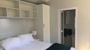 A bedroom with a bed, a nightstand, a lamp, a wardrobe, and a door leading to a bathroom. - Lake Hawea Lakefront Cabin (Lake Hawea)