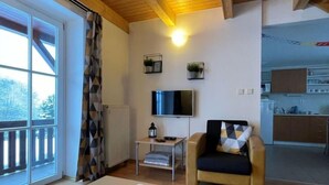 Una sala de estar acogedora con un sofá, un televisor y una mesa con velas. Se observa una ventana con cortinas y vistas al exterior.