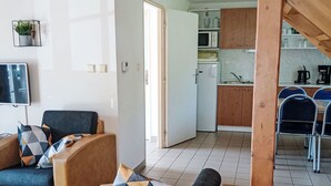 Una sala de estar moderna con un sofá, un sillón, una televisión y una zona de cocina con un microondas y armarios.