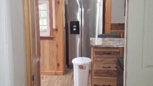 Un couloir étroit mène à une cuisine équipée d’un réfrigérateur en acier inoxydable, de meubles de rangement en bois et d’une fenêtre.