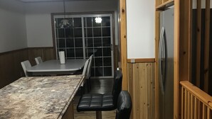 Une cuisine avec un plan de travail en bois, des chaises noires, un réfrigérateur et un coin repas comprenant une table et des chaises.