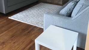 Un salon avec une cheminée en pierre, des canapés gris, une table basse blanche et un tapis à motifs.