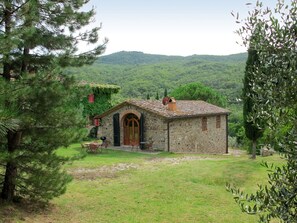 Une maison en pierre avec un toit en tuiles, une porte en bois et un petit patio aménagé avec du mobilier d’extérieur.