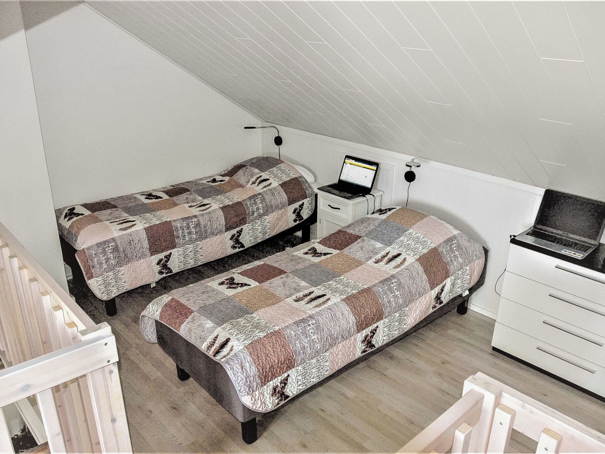 Una habitación pequeña y funcional con dos camas individuales, un escritorio con una computadora portátil, una silla y un aparador.