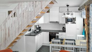 A compact kitchen with a microwave, stove, and sink. A staircase with wooden steps leads to a dining area with a table and chairs.