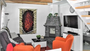 A modern living room with a stone fireplace, orange armchairs, a sofa, and a flat-screen TV.