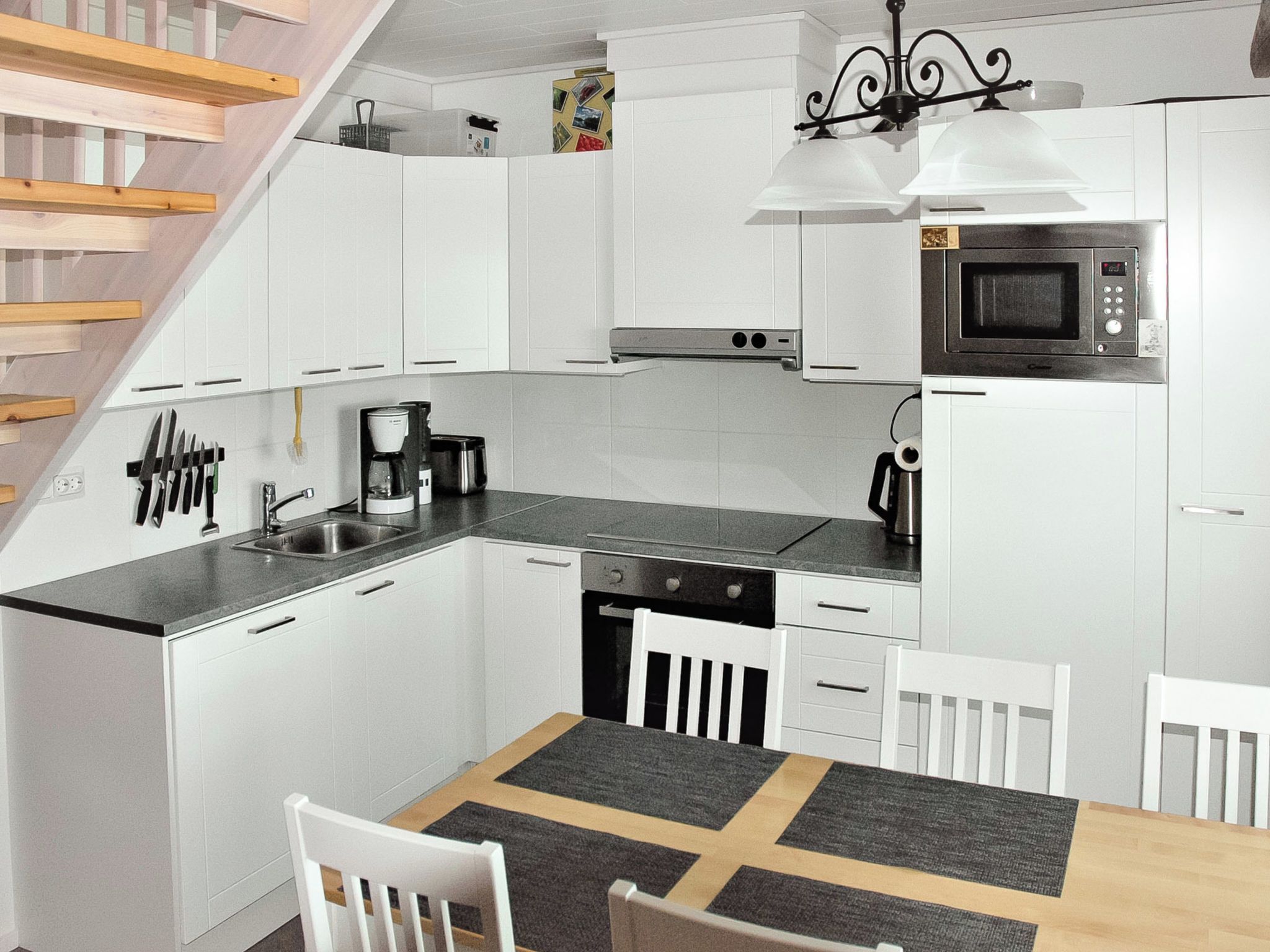 A modern kitchen with white cabinetry, a built-in microwave, a coffee maker, and a dining area with a table and chairs.
