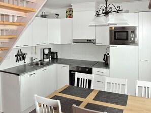 A modern kitchen with white cabinetry, a built-in microwave, a coffee maker, and a dining area with a table and chairs. - Maahisenrinne 3 e 19 by Interhome (Äkäslompolo)