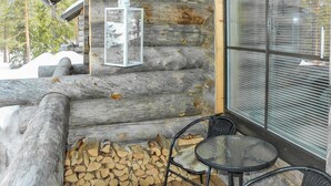 A log cabin with a wooden deck, two chairs, a table, and a lantern.