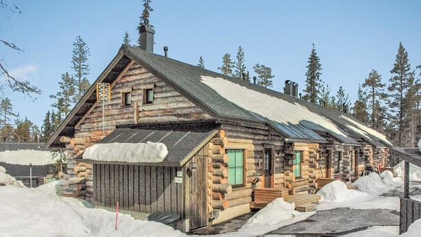 A log cabin with a snow-covered roof, surrounded by snowbanks, and a clear sky.