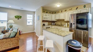 A modern kitchen with white cabinets, a stainless steel refrigerator, and a granite countertop. There is a small island with stools, and a microwave above the stove.
