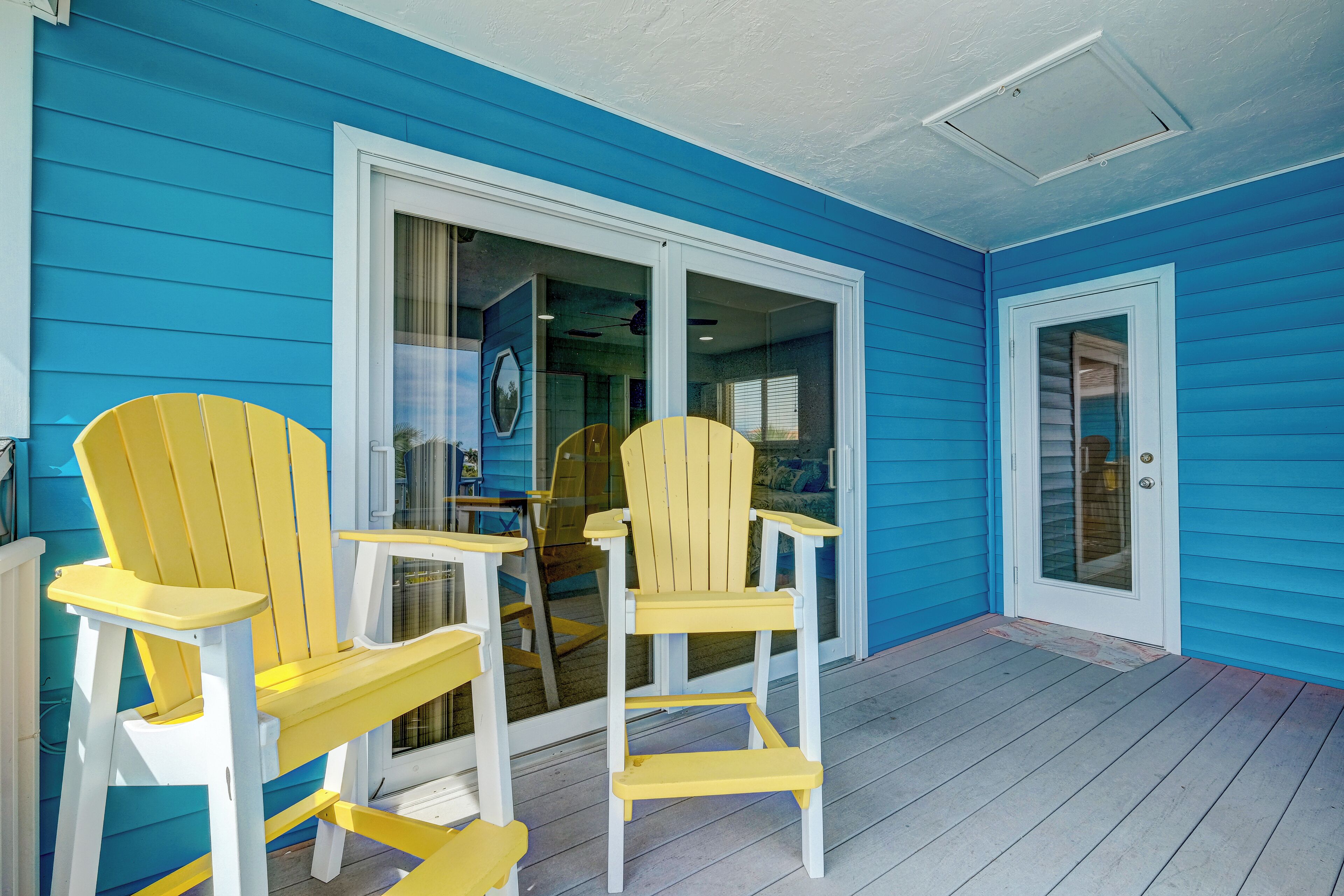 A porch with two yellow Adirondack chairs and a table, blue siding, and a glass door.