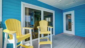 A porch with two yellow Adirondack chairs and a table, blue siding, and a glass door.