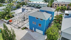 A coastal hotel with multiple buildings, including a prominent blue structure with a balcony, surrounded by palm trees and a view of the ocean.